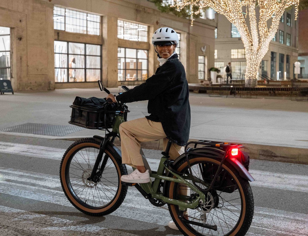 A woman rides a green Radster Trail on a city street at dusk. Her brake lights are on.