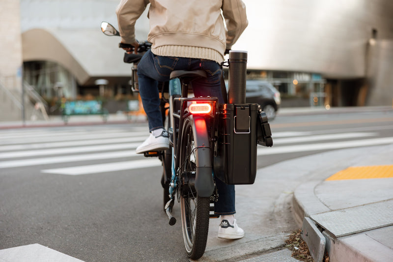Person on a Radster Road electric commuter bike, stopped at a corner showing the brake light in use. 