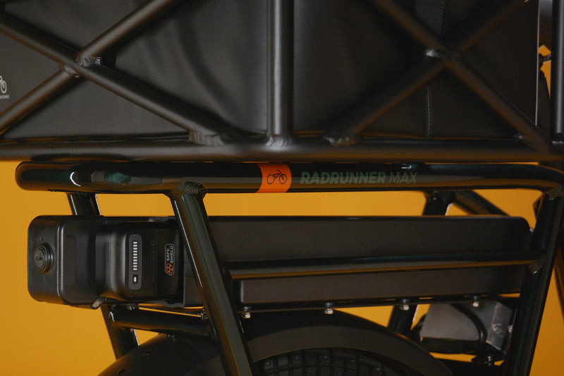 A RadRunner range extender installed on an electric bike under the rear rack against a gold background.