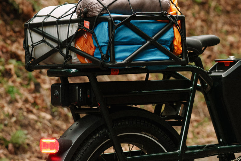 A green ebike with a basket filled with camping gear and a range extender mounted under the rear rack. 
