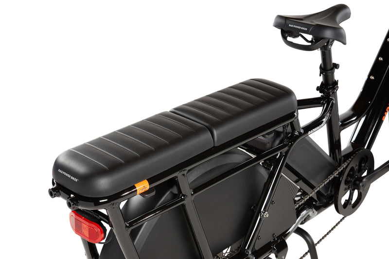Two RadWagon deckpads installed on the back of a RadWagon electric cargo bike, used for passenger seating. Black vinyl material with padding. Subtle Rad Power Bikes logo along the end.