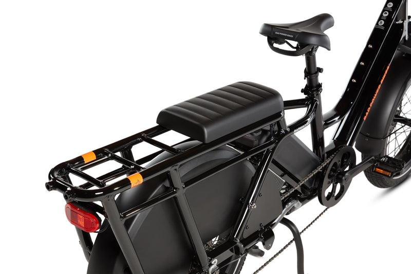 RadWagon deckpad installed in the front-most position on the back of a RadWagon electric cargo bike, used for passenger seating. Black vinyl material with padding. Subtle Rad Power Bikes logo along the end.