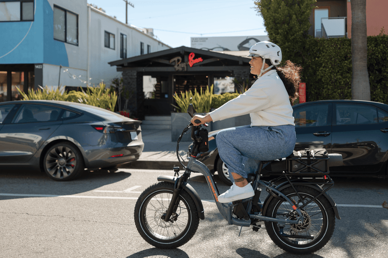 Image of woman riding RadExapnd 5 Plus in Slate Blue riding on the road. She is wearing a helmet. The bike has a Large rear-mounted basket & handlebar bag.